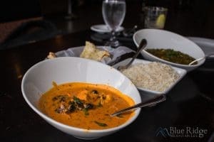 Chicken Tiki Masala in a white bowl with Naan and Basmati rice in the background