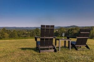 Photo of two outdoor chairs with a glass of wine on a table in the middle with a beautiful view in the distance at Stone Ashe Vineyards Hendersonville NC