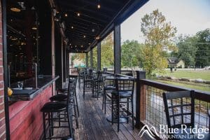 Outside deck at Hillman Beer overlooking the creek.  You can see the bar, and some small tables with chairs.  The deck is covered.