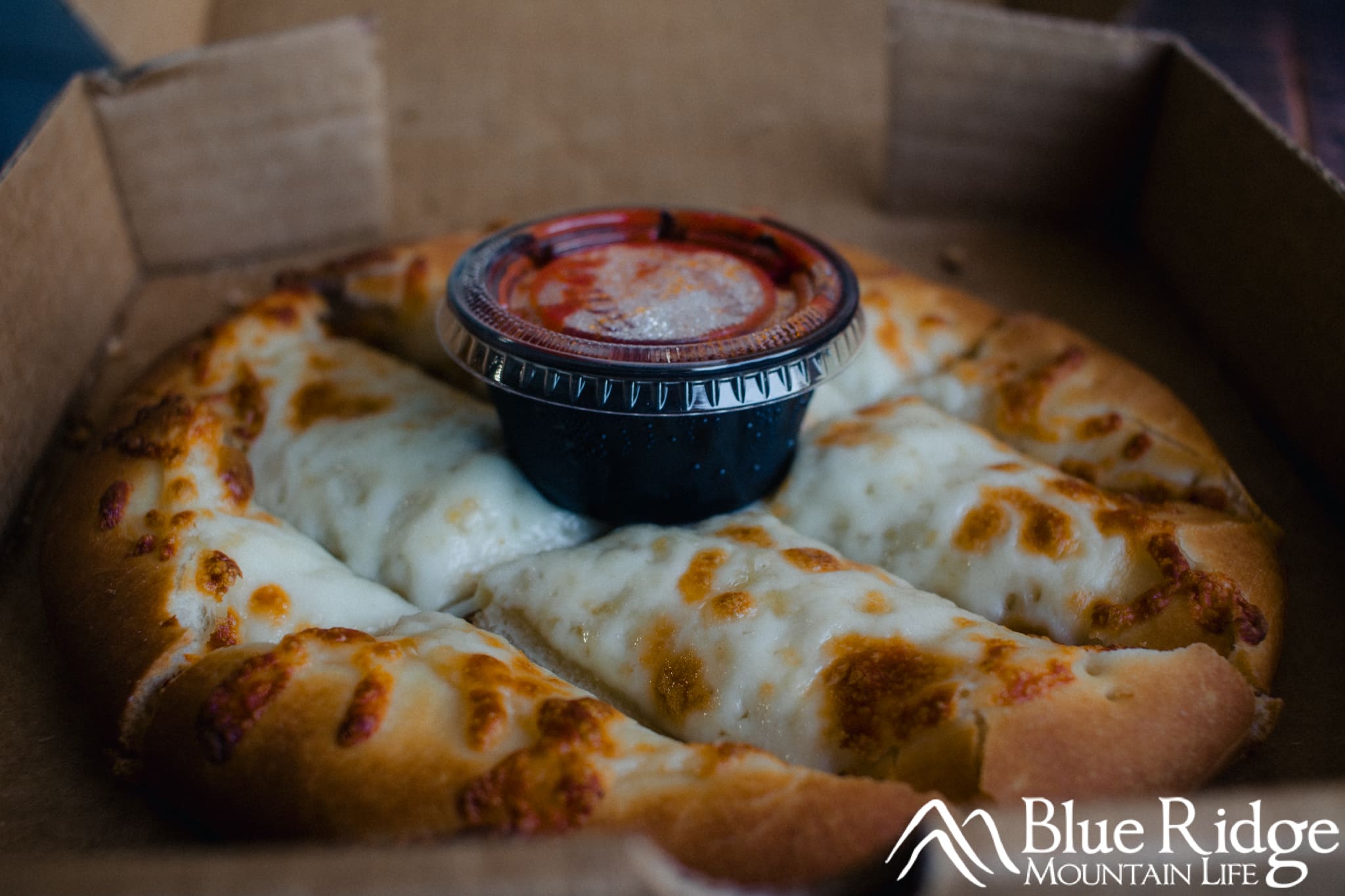 Close up of the cheese sticks, which loks like a small cheese pizza cut up in strips.  Topped with Marinara sauce in a small plastic container