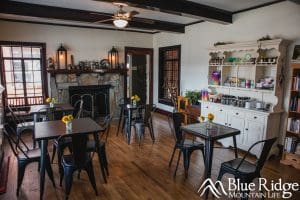 Interior of the Davis Country Store and Cafe showing the main dining area.  There is a old stone fireplace, with small black tables and chairs around it.  The floor is a dark brown hardwood with white walls.