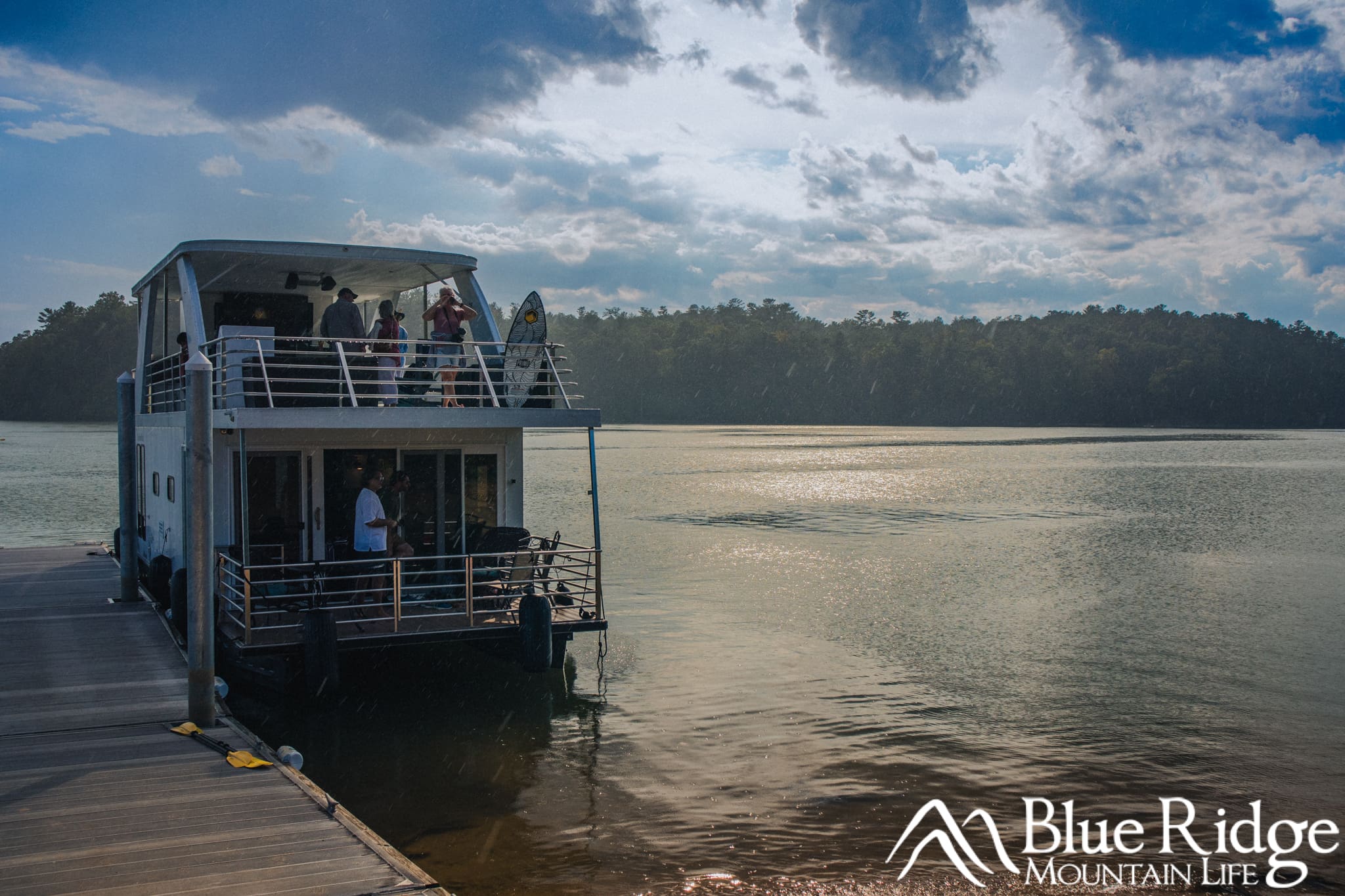 Sunset Boat Tour on Lake James Sunset Boat Tour on Lake James. Photo shows a 2-story house boat docked on the lake. The sun is setting and mountains are in the background.