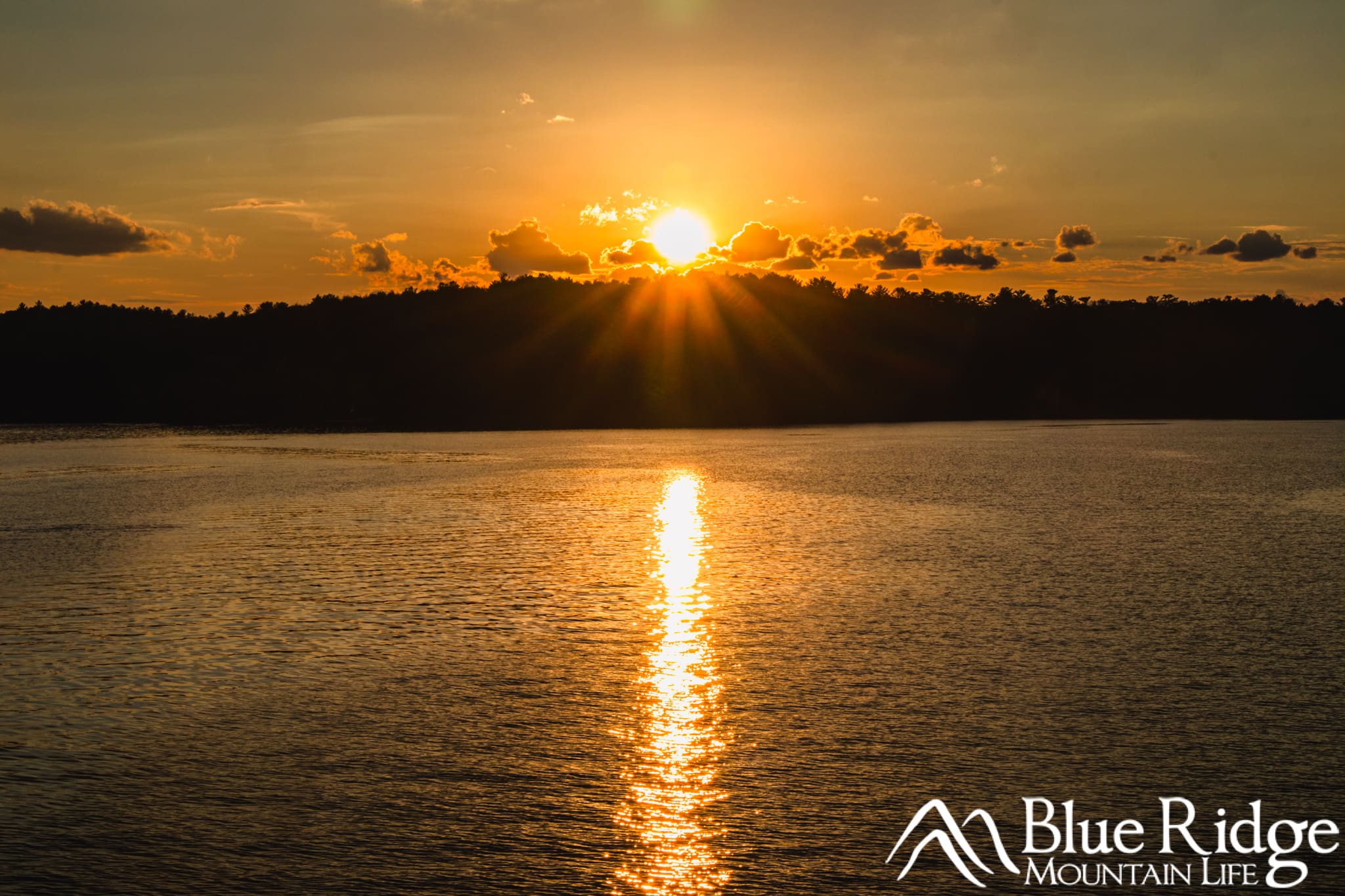 Lake James Sunset Cruise Sunset on Lake James Sunset Cruises. Photo shows the sun just about to drop below the distant mountain peak, with the lake in the foreground reflecting the light.