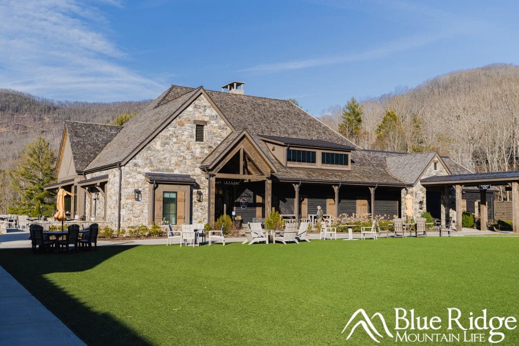 Photo of the main restaurant building for Rocky Face Tavern.  Gray building made from Rock with beautiful green grass in front of it, with mountains in the background.
